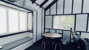 A room with a high ceiling, black and white paneling, a round table with chairs, a bench, and a black leather couch. - Experience Heritage, Live Modern (Upper Hutt)