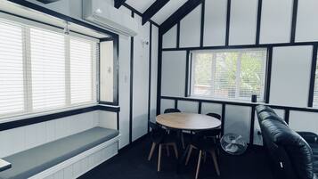 A room with a high ceiling, black and white paneling, a round table with chairs, a bench, and a black leather couch.