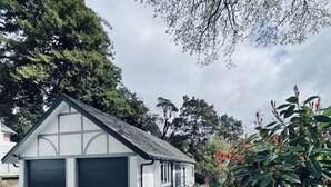 A modern garage with two large doors, surrounded by lush greenery and trees. - Experience Heritage, Live Modern (Upper Hutt)