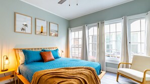 A bedroom with a bed, a chair, a ceiling fan, and a window with curtains.