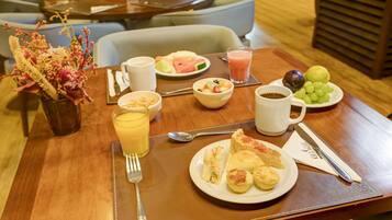 Ein Frühstückstisch mit verschiedenen Speisen, darunter ein Teller mit Gebäck, eine Schale Obst, ein Glas Orangensaft und eine Tasse Kaffee.
