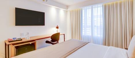 Habitación de hotel con cama, escritorio, silla, televisión y ventana con cortinas.
