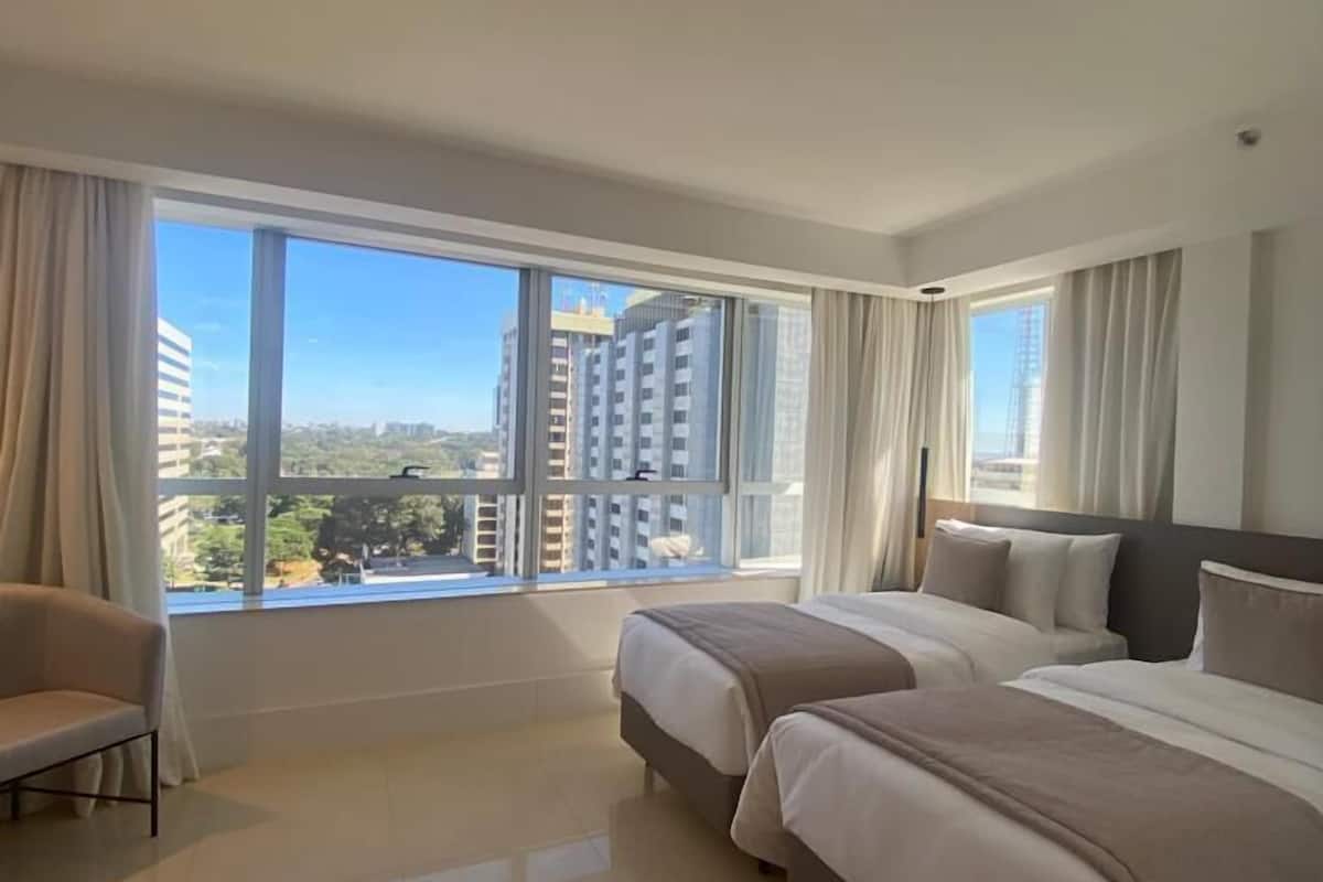 Ein Hotelzimmer mit zwei Betten, einer Couch und großen Fenstern mit Blick auf die Stadt.