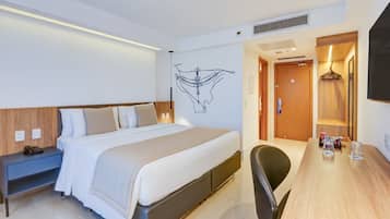 A hotel room with a bed, bedside table, chair, desk, and a wall-mounted artwork.