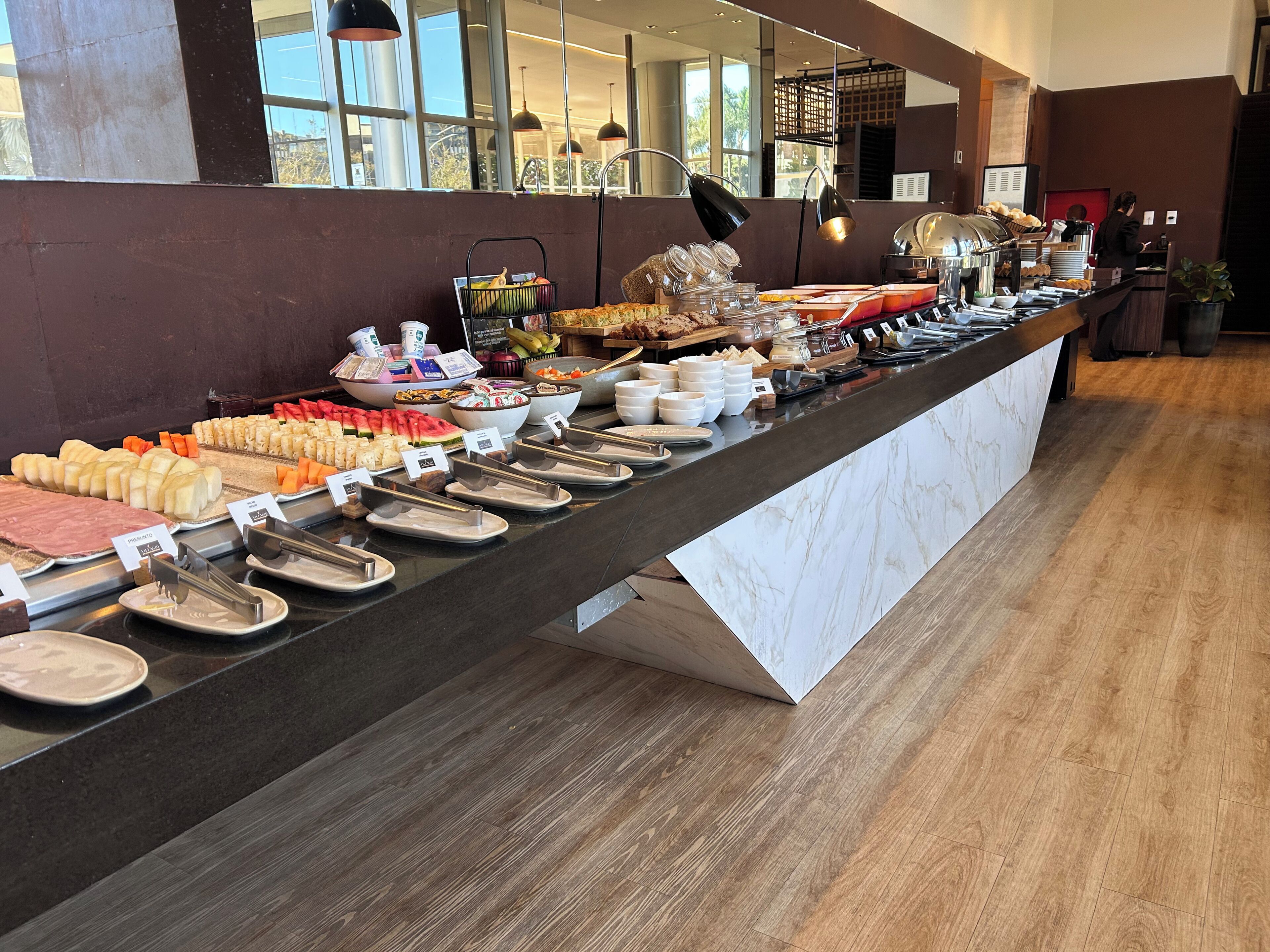 A buffet with various food items and utensils, a counter, and a person in the background.