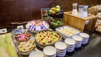 Een buffet met diverse gerechten, waaronder fruit, kazen en verpakte snacks.