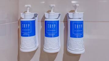 Três dosadores de produtos de higiene pessoal brancos da TRYP by Wyndham numa parede revestida a azulejos.