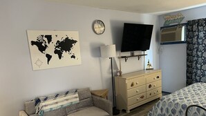 Un dormitorio con un mapa mundial, un televisor, un aparador, una cama y una ventana con cortinas.