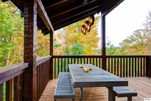 Une terrasse en bois avec une table de pique-nique et des bancs, entourée d’arbres aux feuilles d’automne.