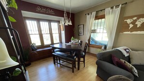 A dining area with a wooden table and chairs, a sofa, and a large window with curtains.
