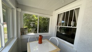 A small, enclosed patio area with a table and chairs, a pitcher, and large windows offering views of the outdoors.