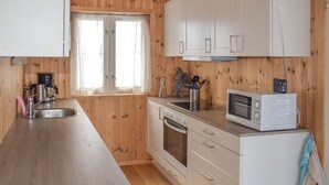 A compact kitchen with wooden walls, a stainless steel sink, a coffee maker, a microwave, and a small oven. - Gorgeous home in Noresund with WiFi (Noresund)