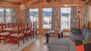 A cozy room with wooden walls, a dining table with chairs, a sofa, and large windows with a snowy mountain view. - Gorgeous home in Noresund with WiFi (Noresund)