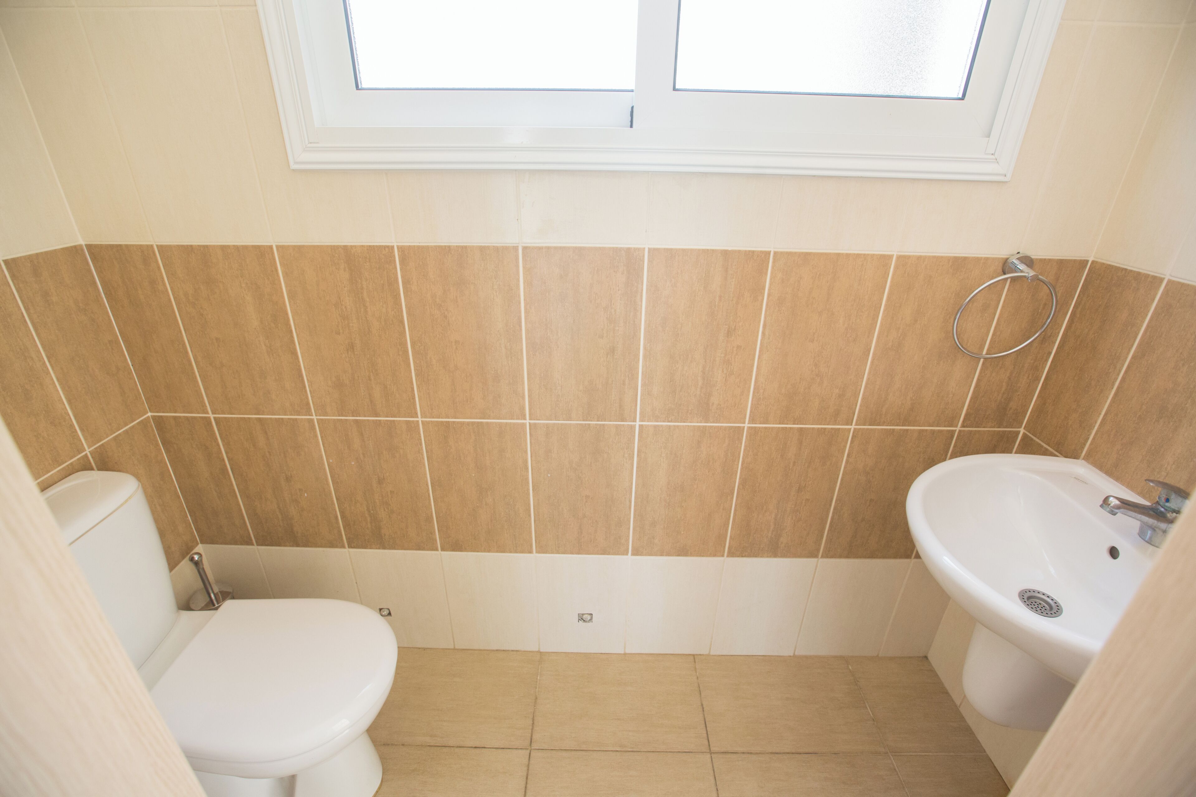 Un baño con inodoro, lavamanos y una ventana sobre el lavamanos.