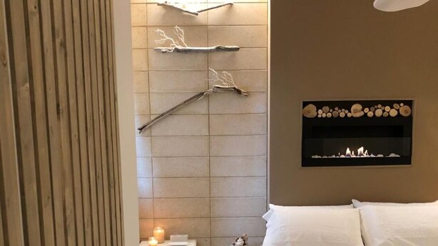 Een slaapkamer met een bed, nachtkastje, wandplank en een wandhaard.