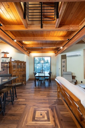 Interior de madeira com área de jantar, um banco e vista pela janela.