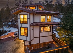 A multi-story building with a traditional architectural style, featuring a combination of white and dark wood paneling, multiple windows with warm lighting, and a wooden deck area. - Beautiful Japanese Pagoda (Bend)