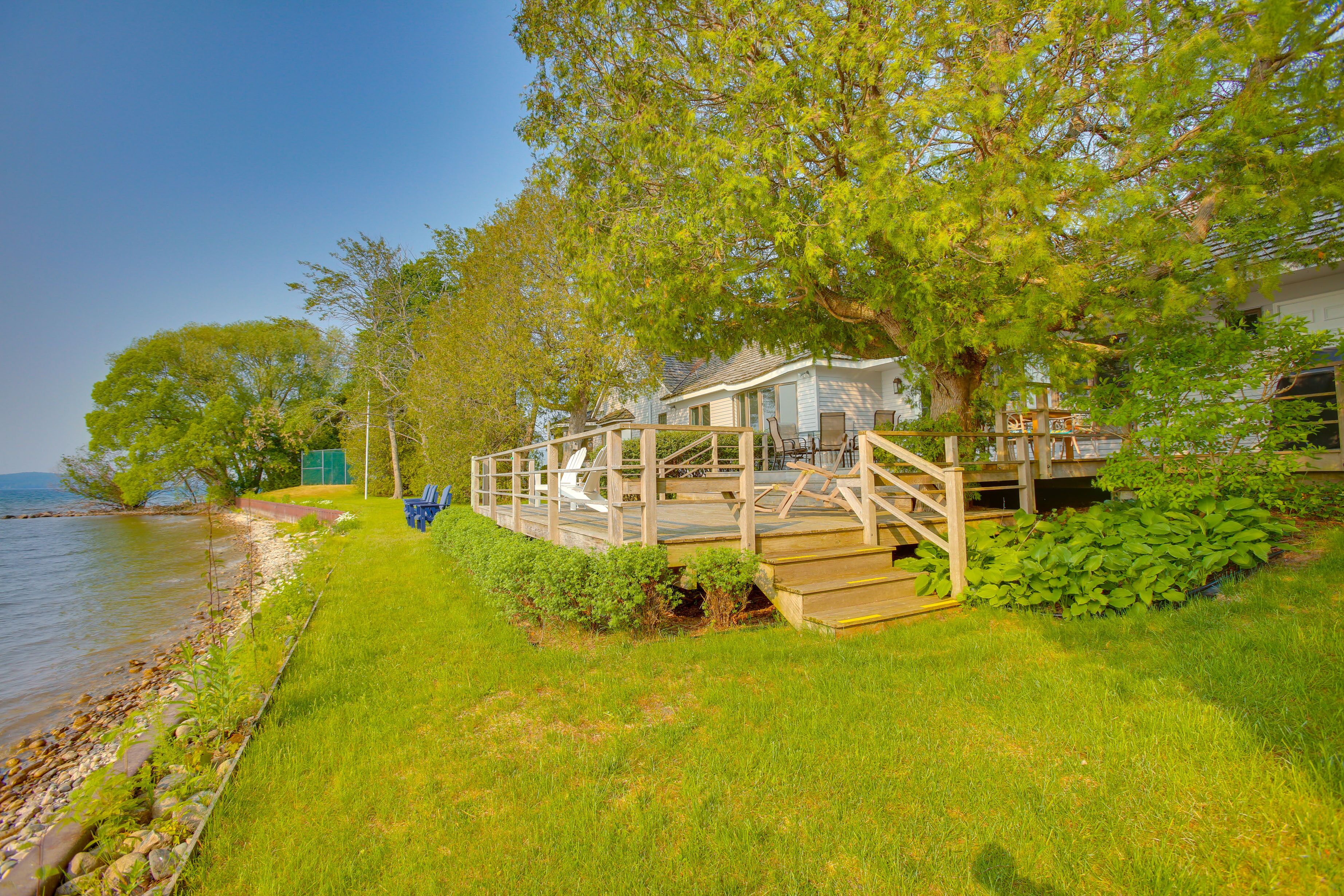 A lakeside cabin with a deck, surrounded by lush greenery and a clear view of the lake.