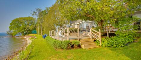 A lakeside cabin with a deck, surrounded by lush greenery and a clear view of the lake.