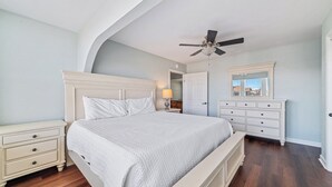 Ein Schlafzimmer mit einem großen Bett, einem Nachttisch, einer Kommode und einem Deckenventilator.