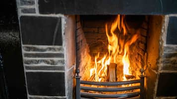 A fireplace with a fire burning inside, surrounded by a brick wall.