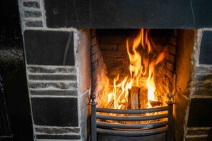 A fireplace with a fire burning inside, surrounded by a brick wall.