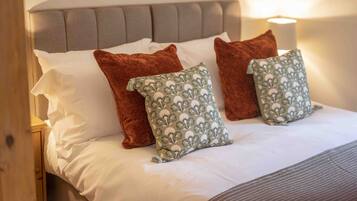 A neatly made bed with white linens, a grey upholstered headboard, and three pillows: two brown and one with a floral pattern.