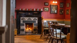A cozy room with a fireplace, wooden flooring, and a seating area with chairs and a table.