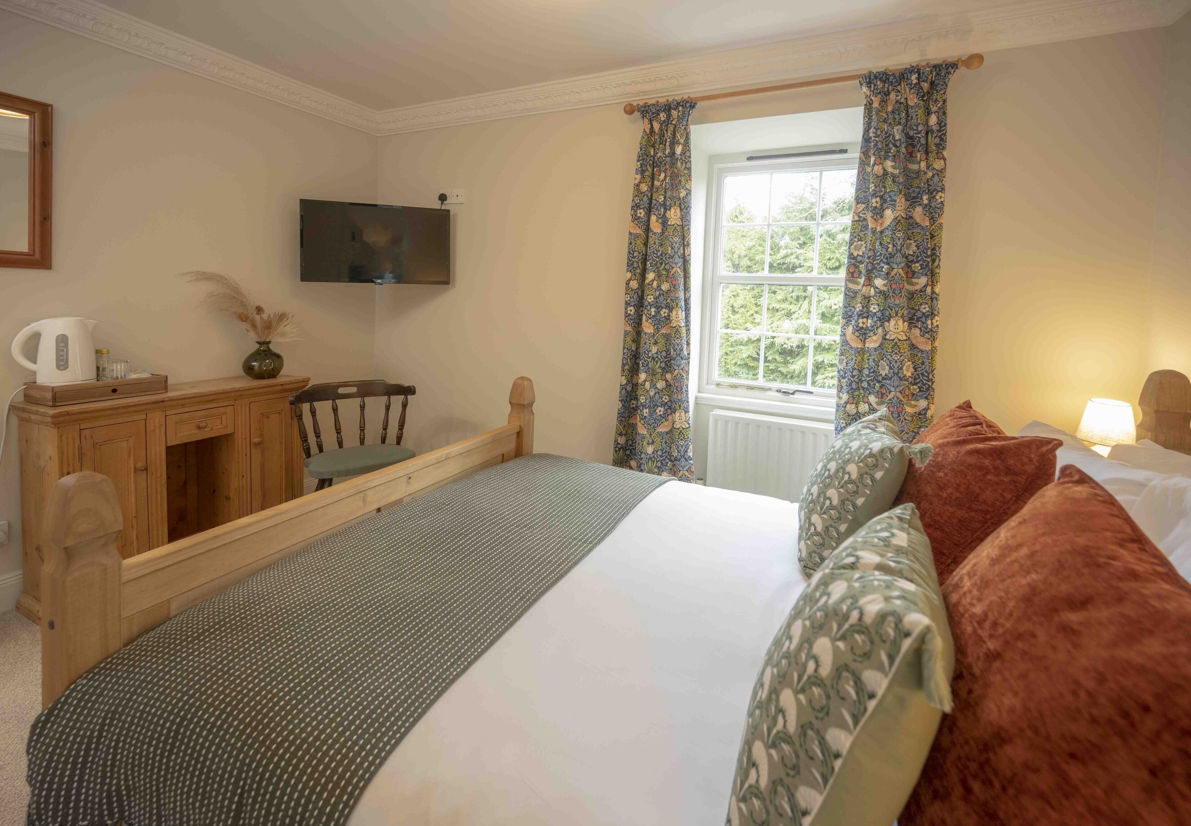 A bedroom with a bed, a wooden desk, a chair, a television, and a window with curtains.