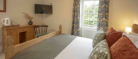 A bedroom with a bed, a wooden desk, a chair, a television, and a window with curtains.