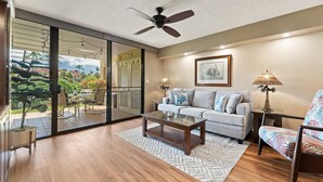 Un salón amplio con puerta corredera de vidrio que da a un patio, ventilador de techo, sofá, mesa de centro y lámpara.