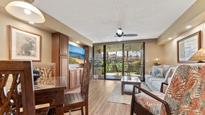Un amplio espacio habitable con una mesa de comedor de madera, un sofá estampado con motivos tropicales y un ventilador de techo.