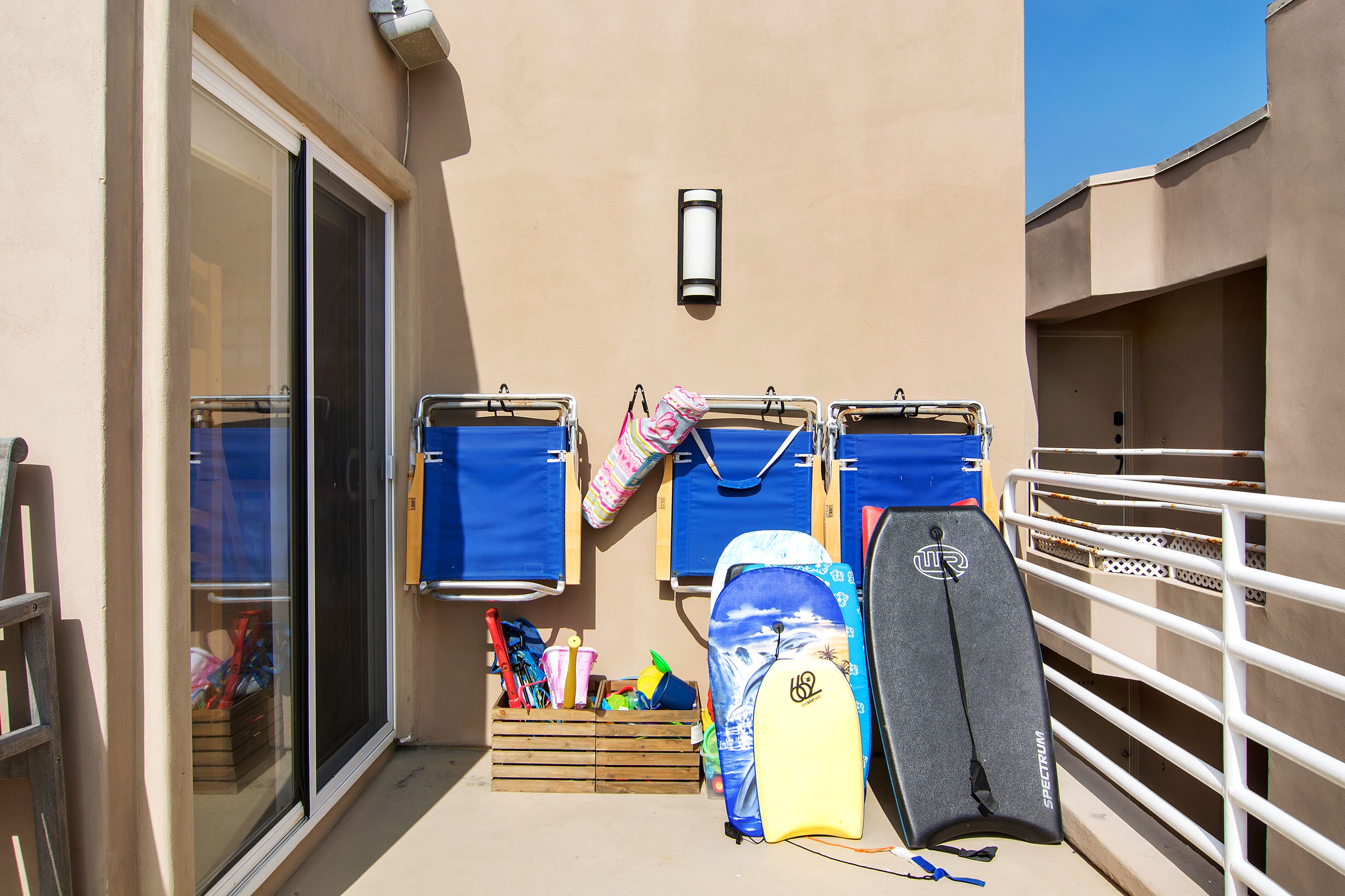 Ein Balkon mit einem Surfbrett, einer Aufbewahrungsbox mit diversen Gegenständen und einem Geländer.