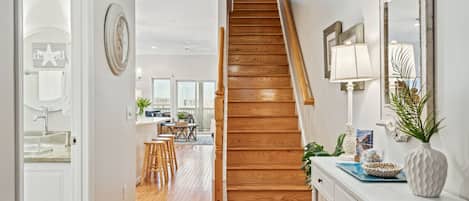 A hallway leading to a wooden staircase, a kitchen area with a dining table, and a bathroom with a starfish decoration.