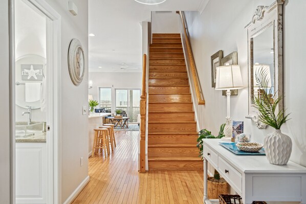 A hallway leading to a wooden staircase, a kitchen area with a dining table, and a bathroom with a starfish decoration.