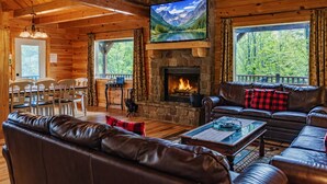 A cozy cabin interior with a stone fireplace, leather sofas, and a dining area with chairs. - Hidden Lake Lodge: Lake + 30 Acres Hocking Hills (Logan)