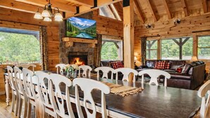 A wooden cabin interior with a dining table, chairs, a fireplace, a sofa, and a television. - Hidden Lake Lodge: Lake + 30 Acres Hocking Hills (Logan)