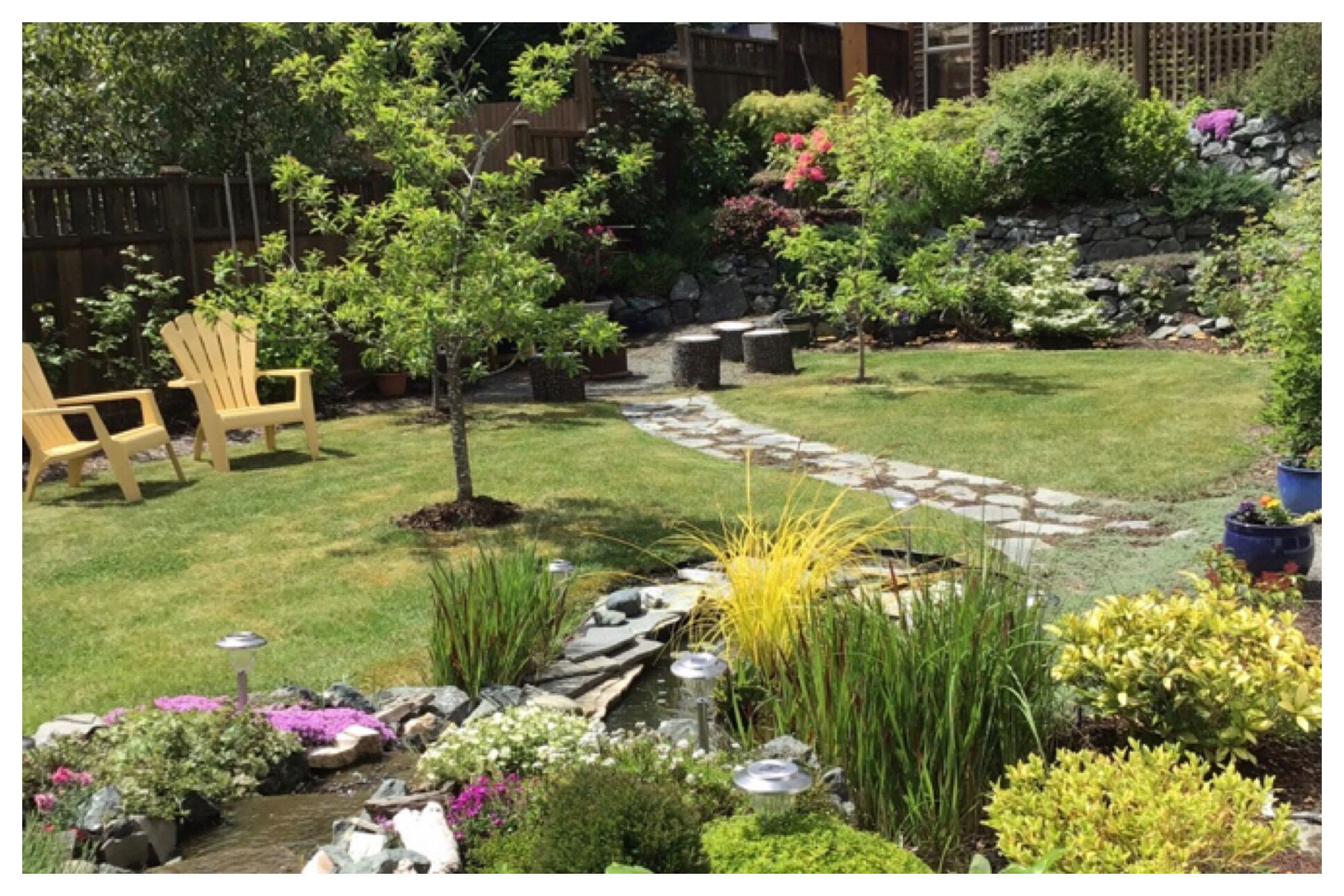 A well-maintained garden with a stone pathway, a small water feature, and various plants and flowers.