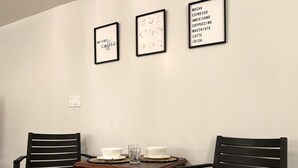 Un coin repas comprenant deux chaises noires, une table en bois et trois tableaux encadrés accrochés au mur.