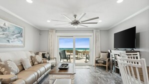 Una sala de estar con un sofá de cuero, una mesa de centro y un televisor. Hay un balcón con vista a la playa.