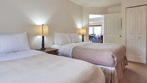 A hotel room with two beds, a nightstand with a lamp, and a door leading to a hallway. - Ocean Front Condo (Parksville)