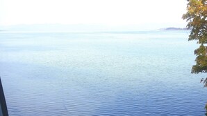 A view from a window overlooking a calm sea with a rocky shoreline and a distant landmass. - Ocean Front Condo (Parksville)
