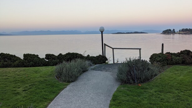 A pathway leading to a bench overlooking a calm lake with distant mountains. - Ocean Front Condo (Parksville)