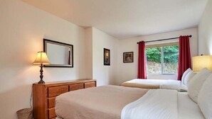 A hotel room with two beds, a wooden dresser, a lamp, and a window with red curtains. - Ocean Front Condo (Parksville)