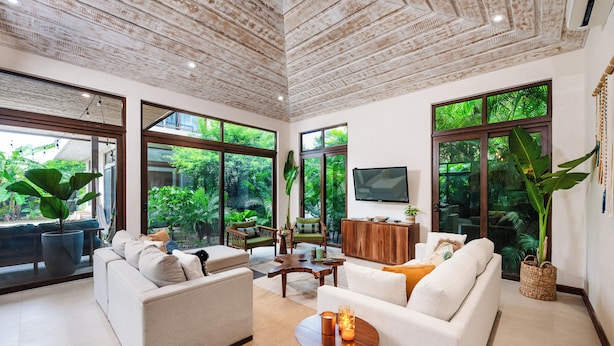 Amplia sala de estar con ventanas grandes, techo de madera y televisor.