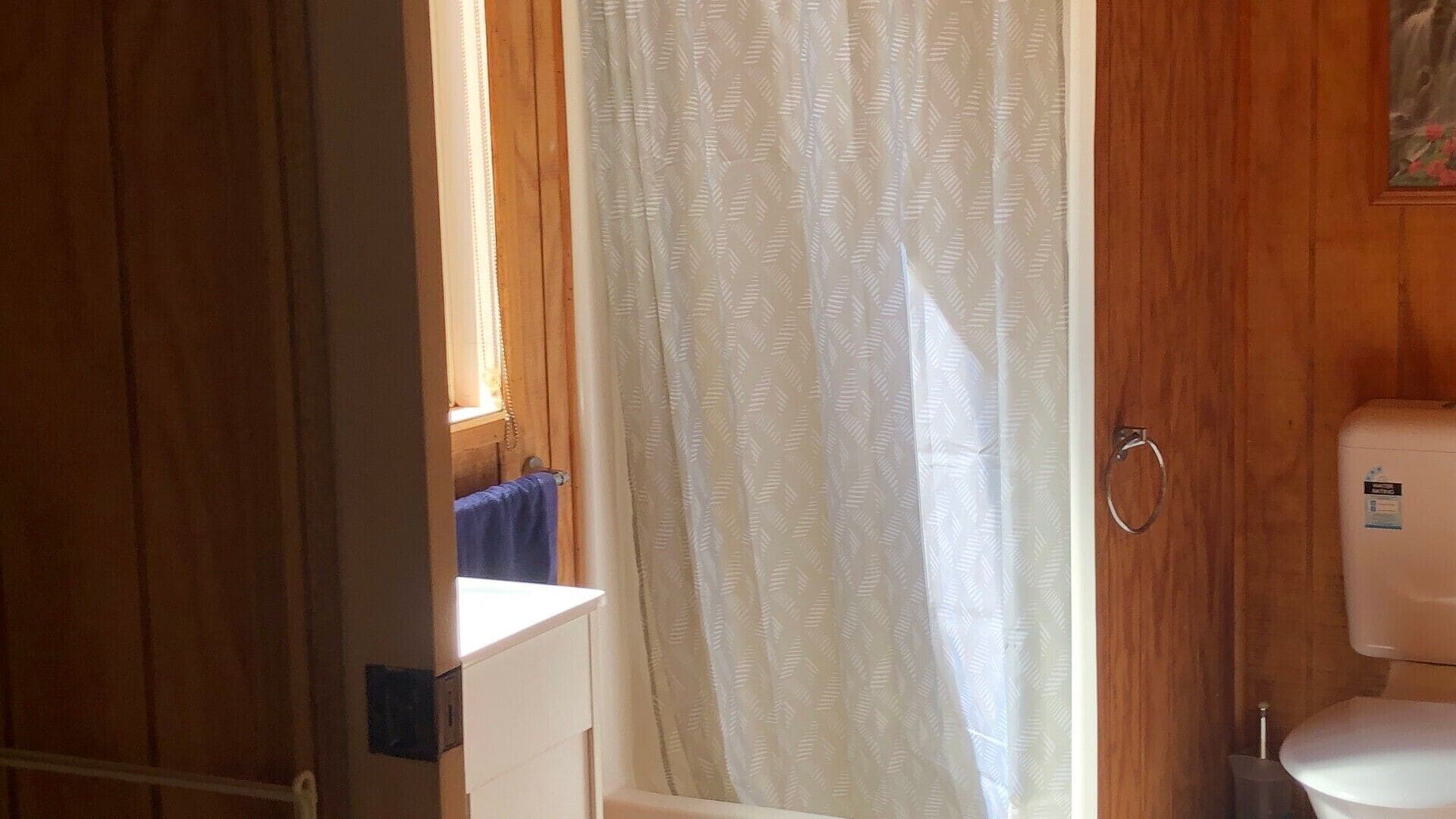 A bathroom with a toilet, a shower curtain, and wooden walls.