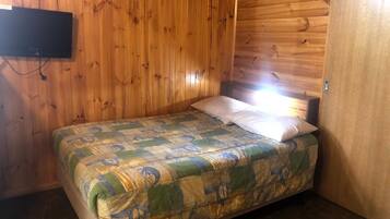 A small wooden room with a bed, a television mounted on the wall, and a door.