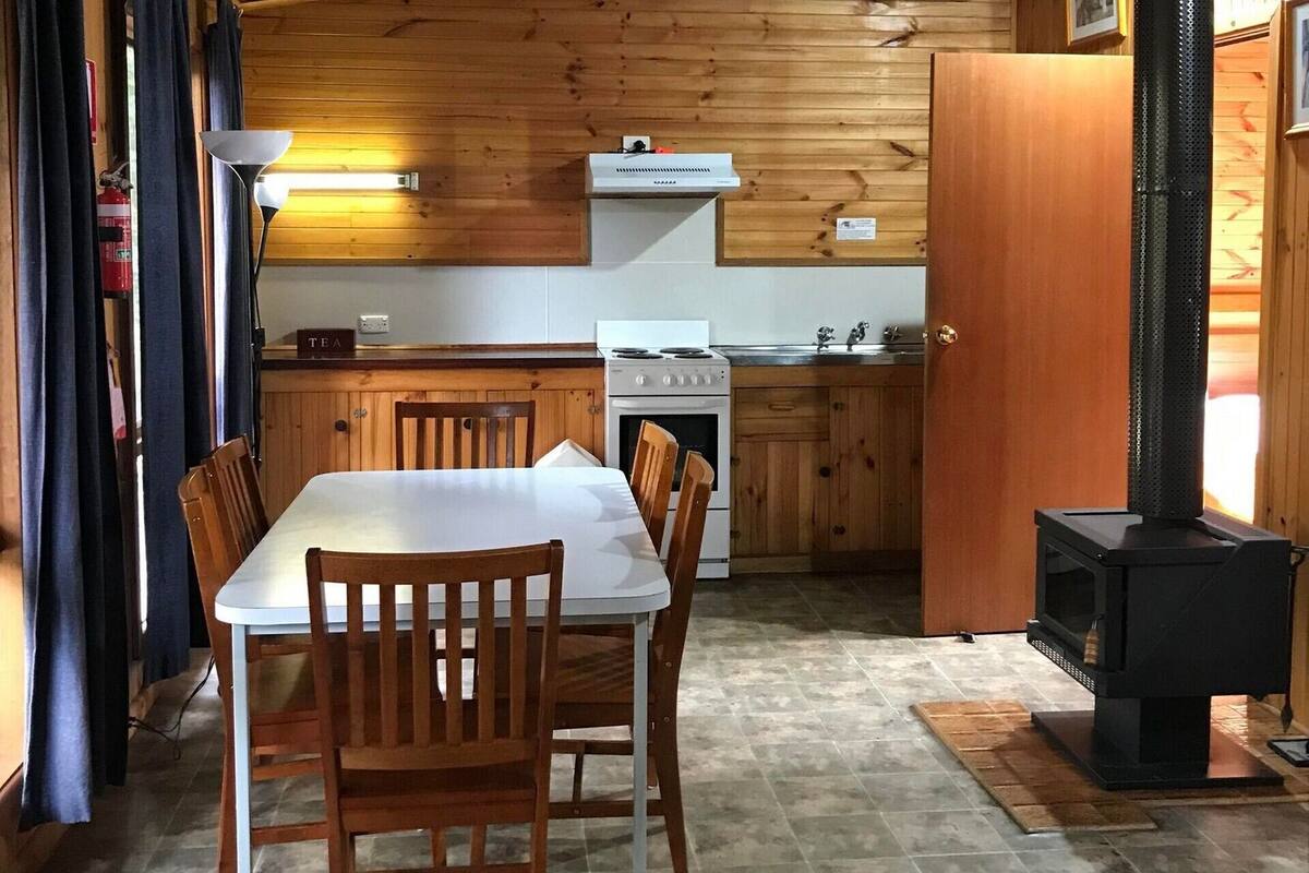 A compact kitchen with wooden cabinets, a white stove, and a black wood-burning stove.