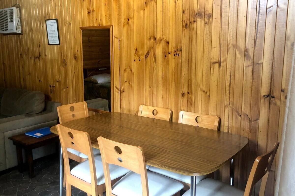 A wooden interior with a dining table and chairs, a sofa, and a small table with a laptop.