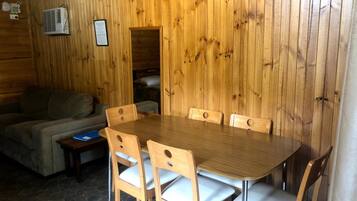 Un intérieur en bois comprenant une table à manger et des chaises, un canapé et une petite table sur laquelle se trouve un ordinateur portable.